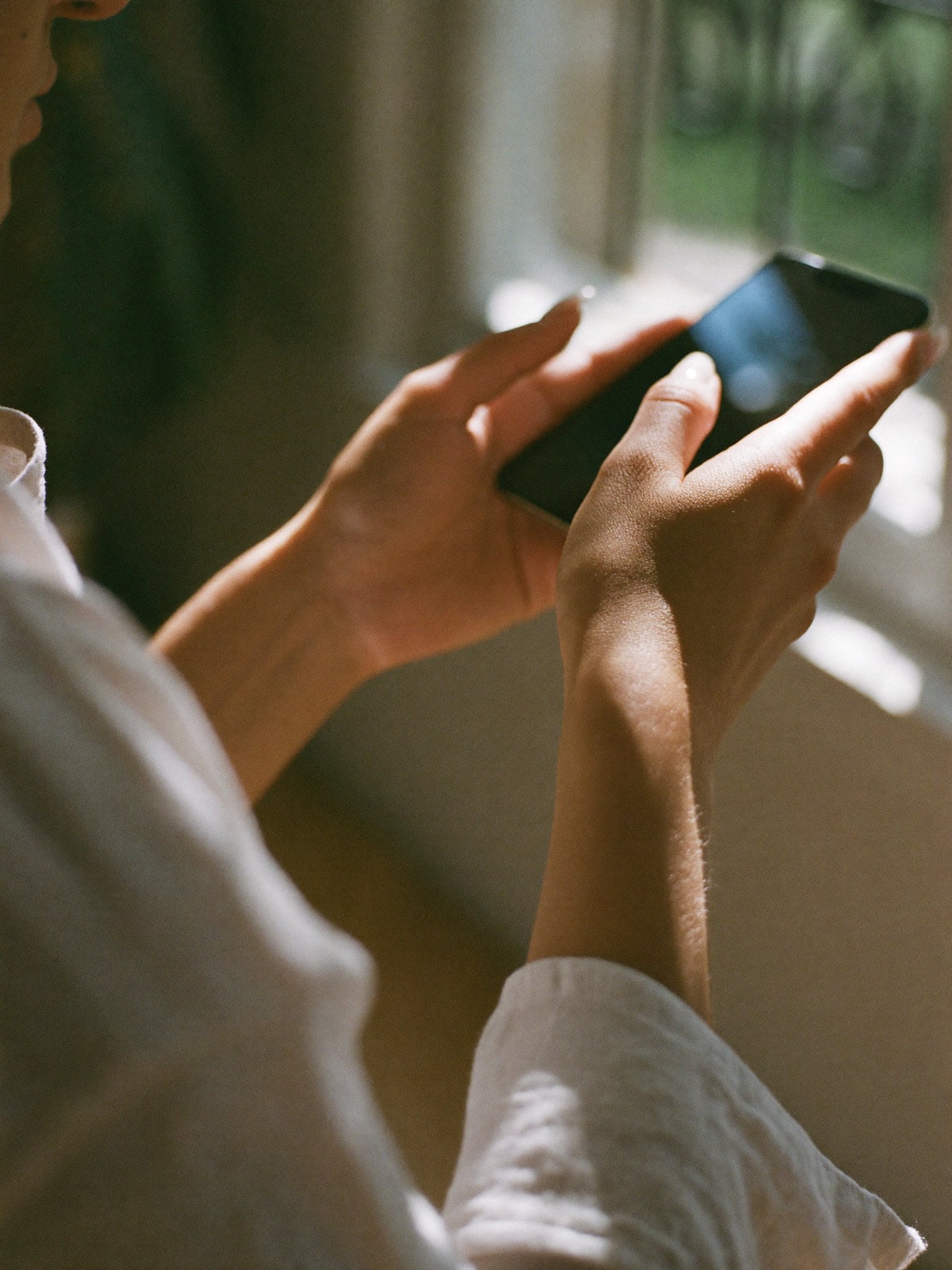 Las manos de una candidata con su celular, junto a una ventana con sol.