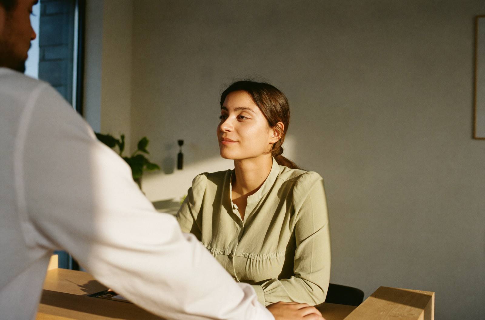 Una recepcionista escucha con calma a una persona frente a su escritorio, con la luz de la tarde.