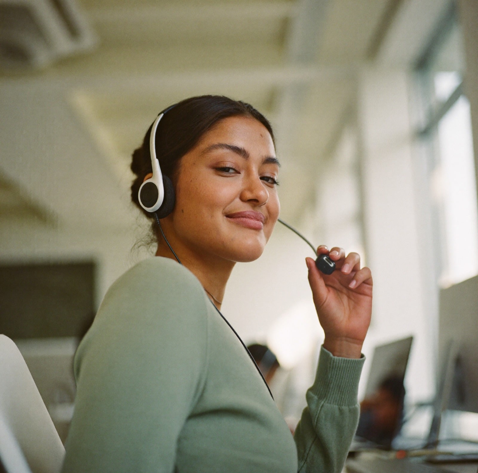 Una agente de call center escucha con su diadema puesta, en su lugar junto a una ventana.